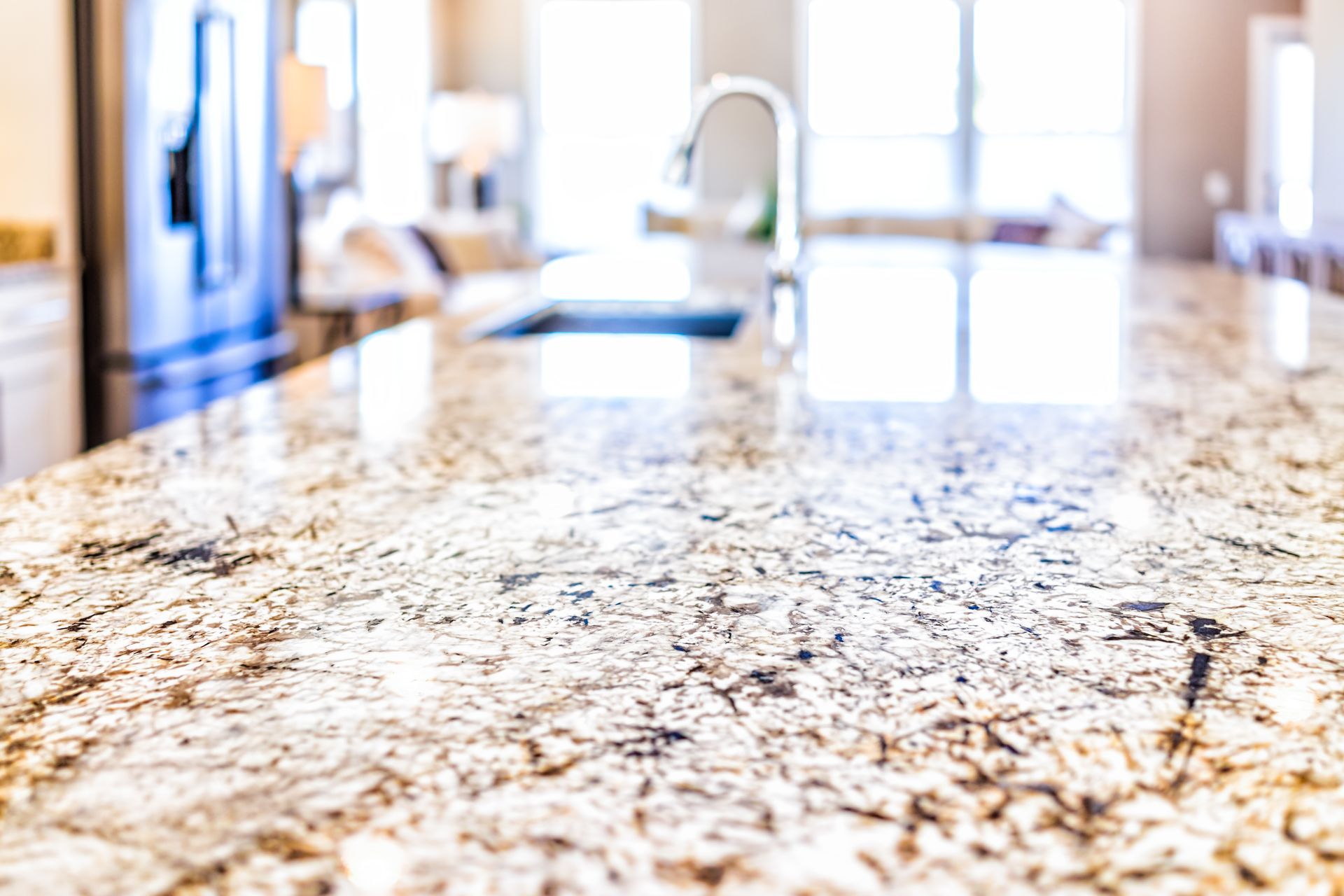 Bright kitchen island with speckled granite countertop and a blurred faucet in the background