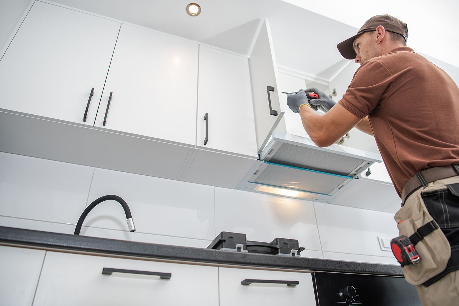 Technician installing a range hood in a modern white kitchen.