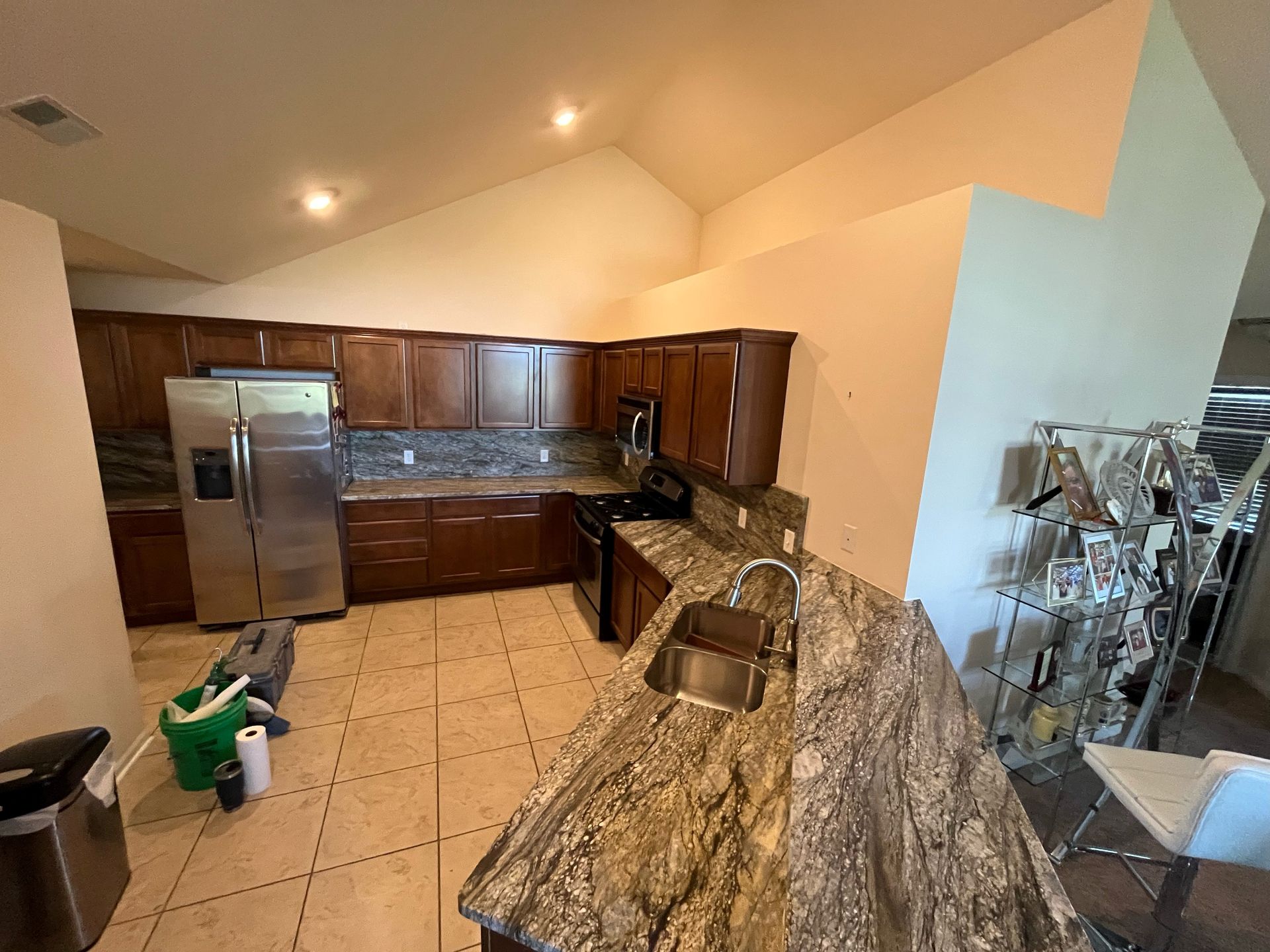 A kitchen with dark wood cabinets, stainless steel appliances, speckled granite countertops, and light tile flooring.