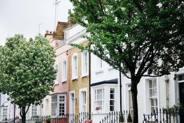 Row of pastel townhouses with black iron fences and leafy trees along a quiet street