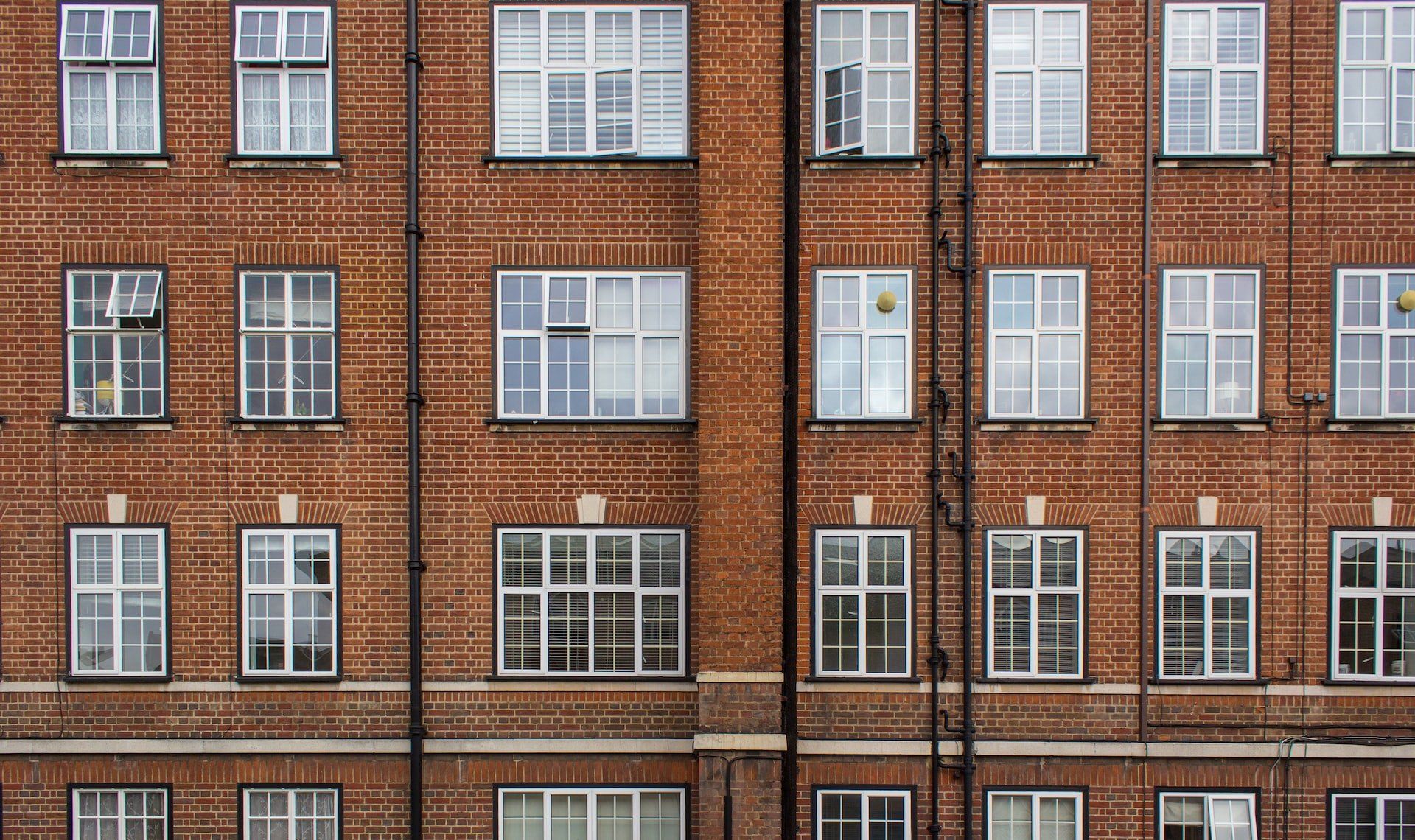 Brick apartment building facade with rows of white-framed windows and brick columns