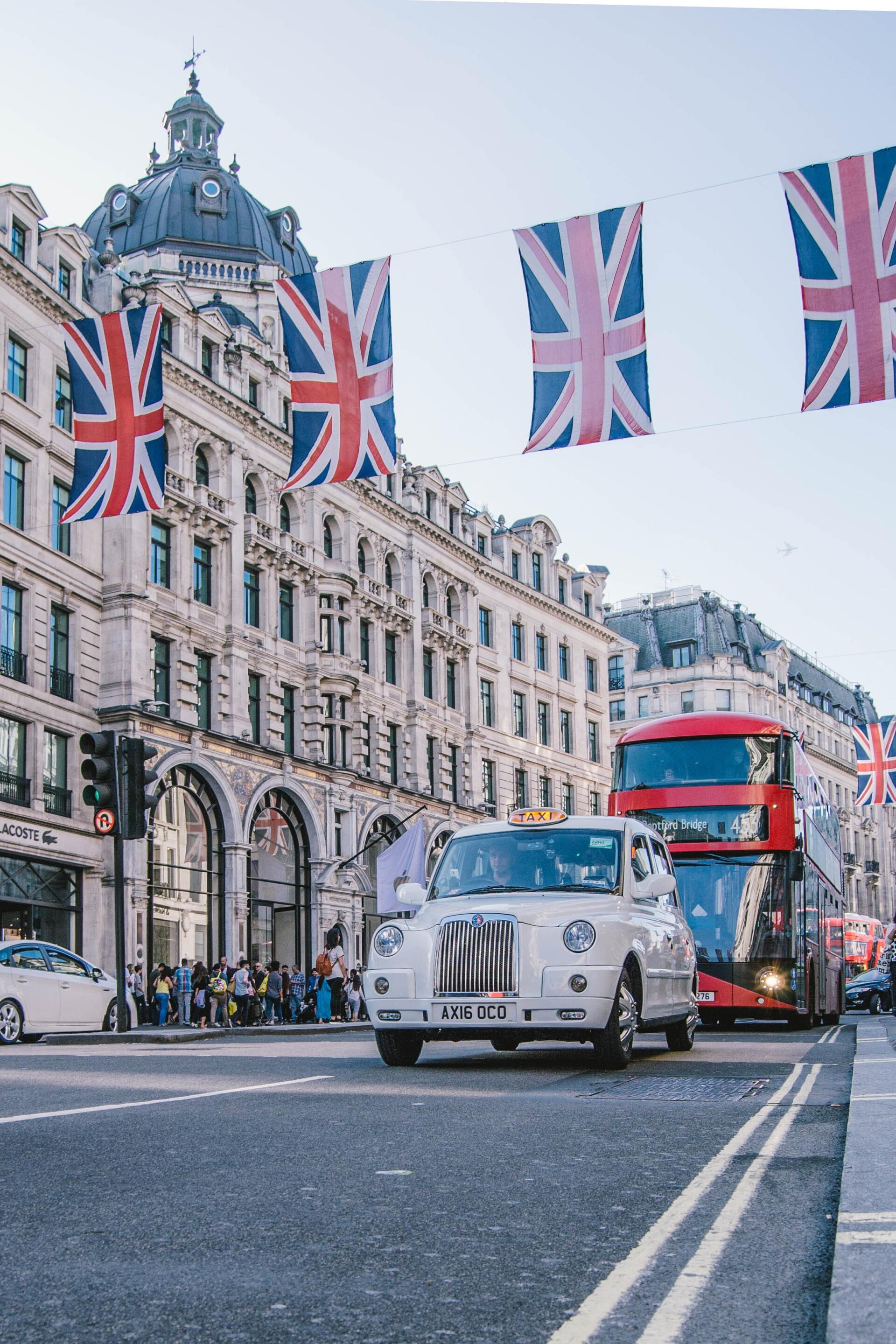 Red double-decker bus and vintage taxi on a London street with Union Jack flags overhead