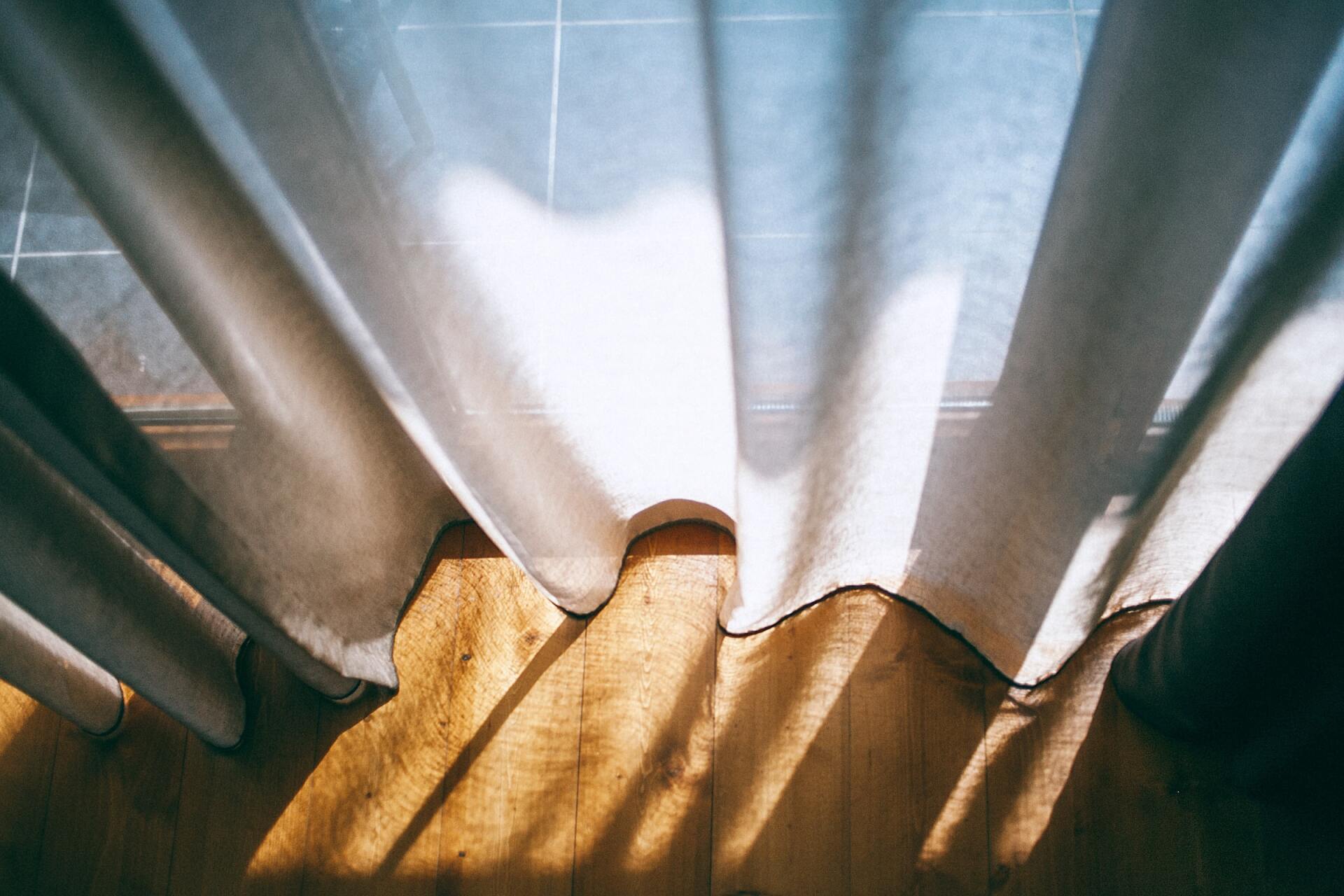 Sunlight casting soft shadows on white curtains over a wooden floor