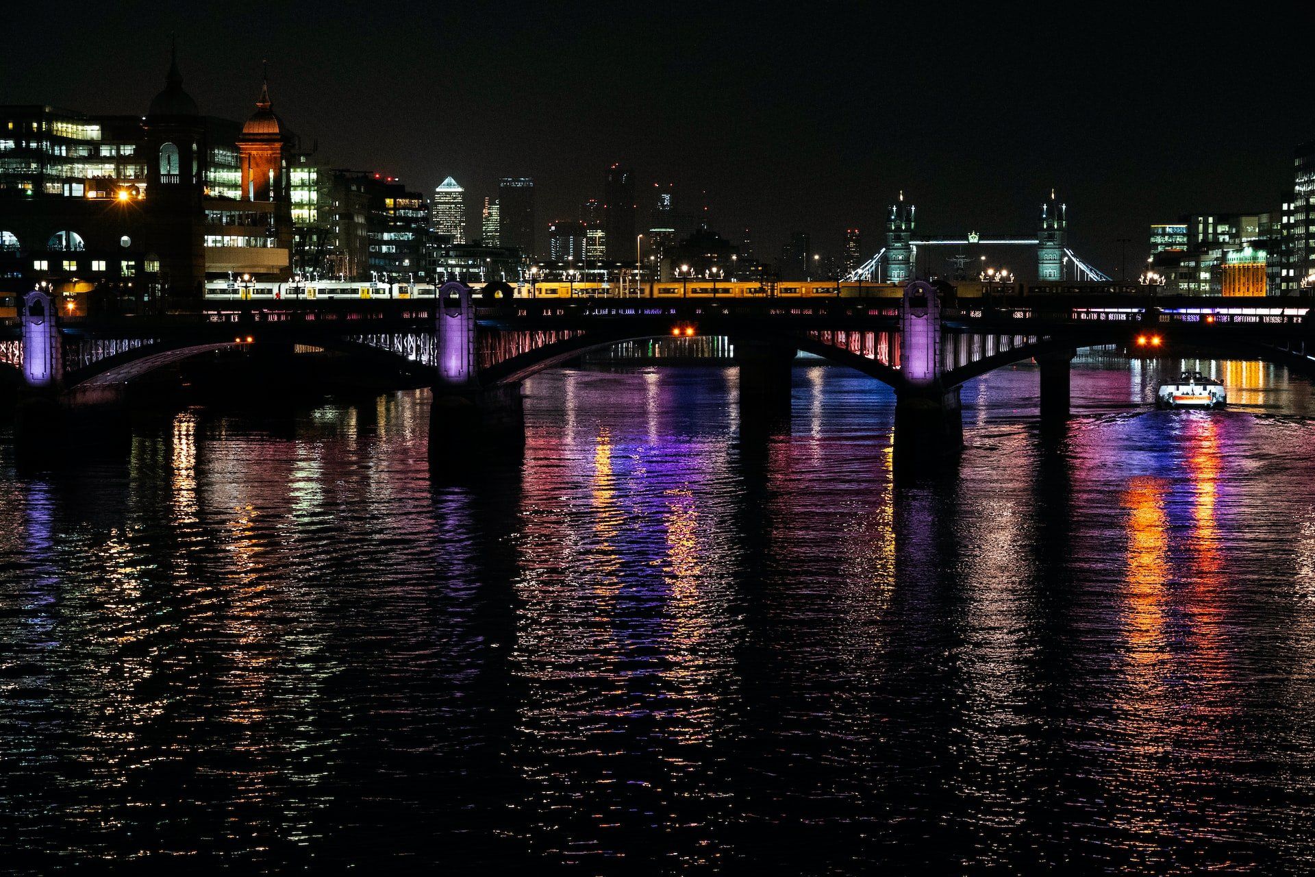 Night city bridge over a river, glowing purple and orange lights reflecting on the water