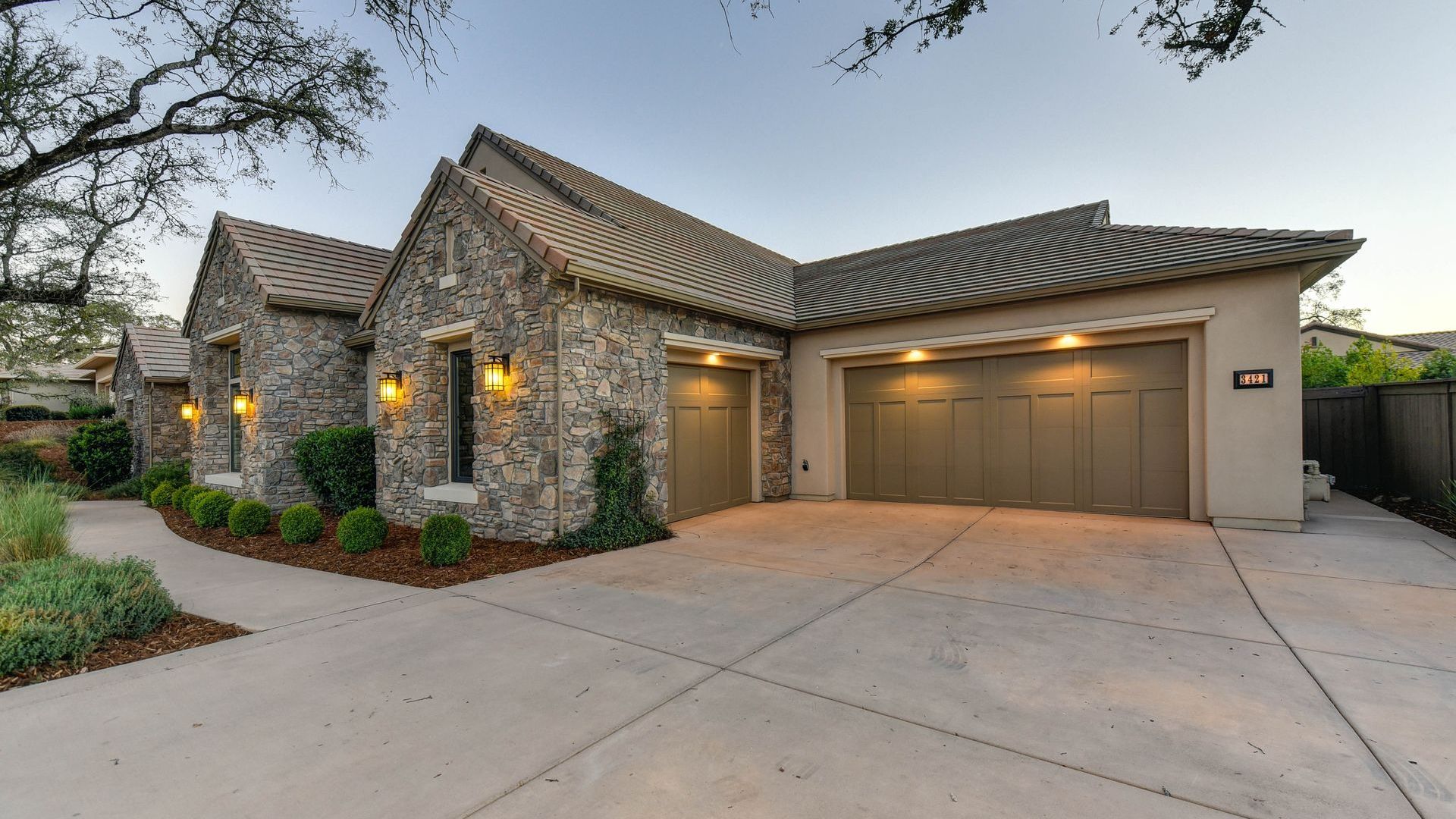 A large stone house with two garage doors and a concrete driveway
