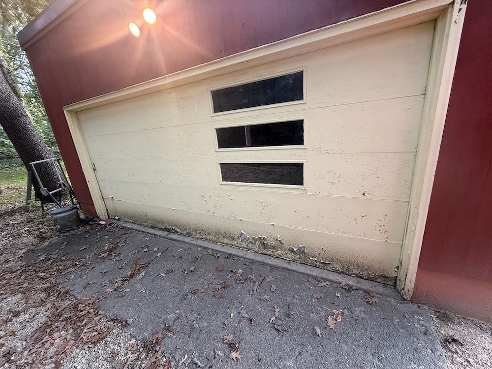 A white garage door with three windows is sitting next to a red building.