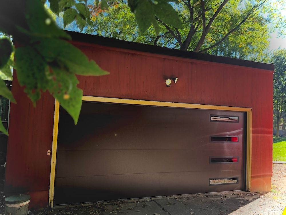 A red garage with a brown door is surrounded by trees.