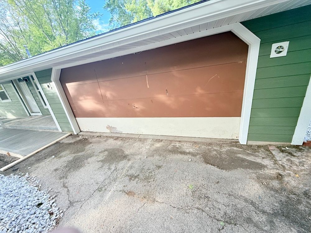 A brown garage door with a green siding on a house.