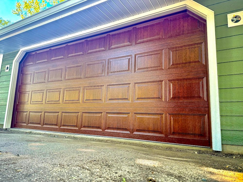 A large wooden garage door is sitting on the side of a green house.