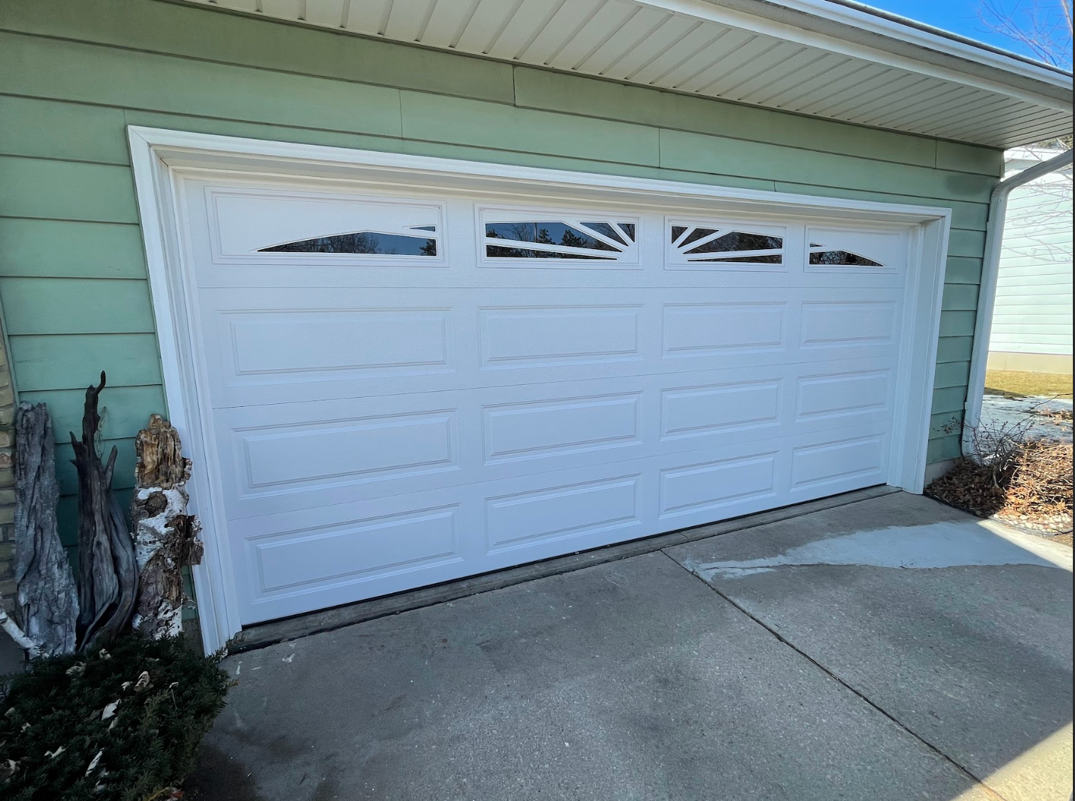 A white garage door is sitting in front of a green house.