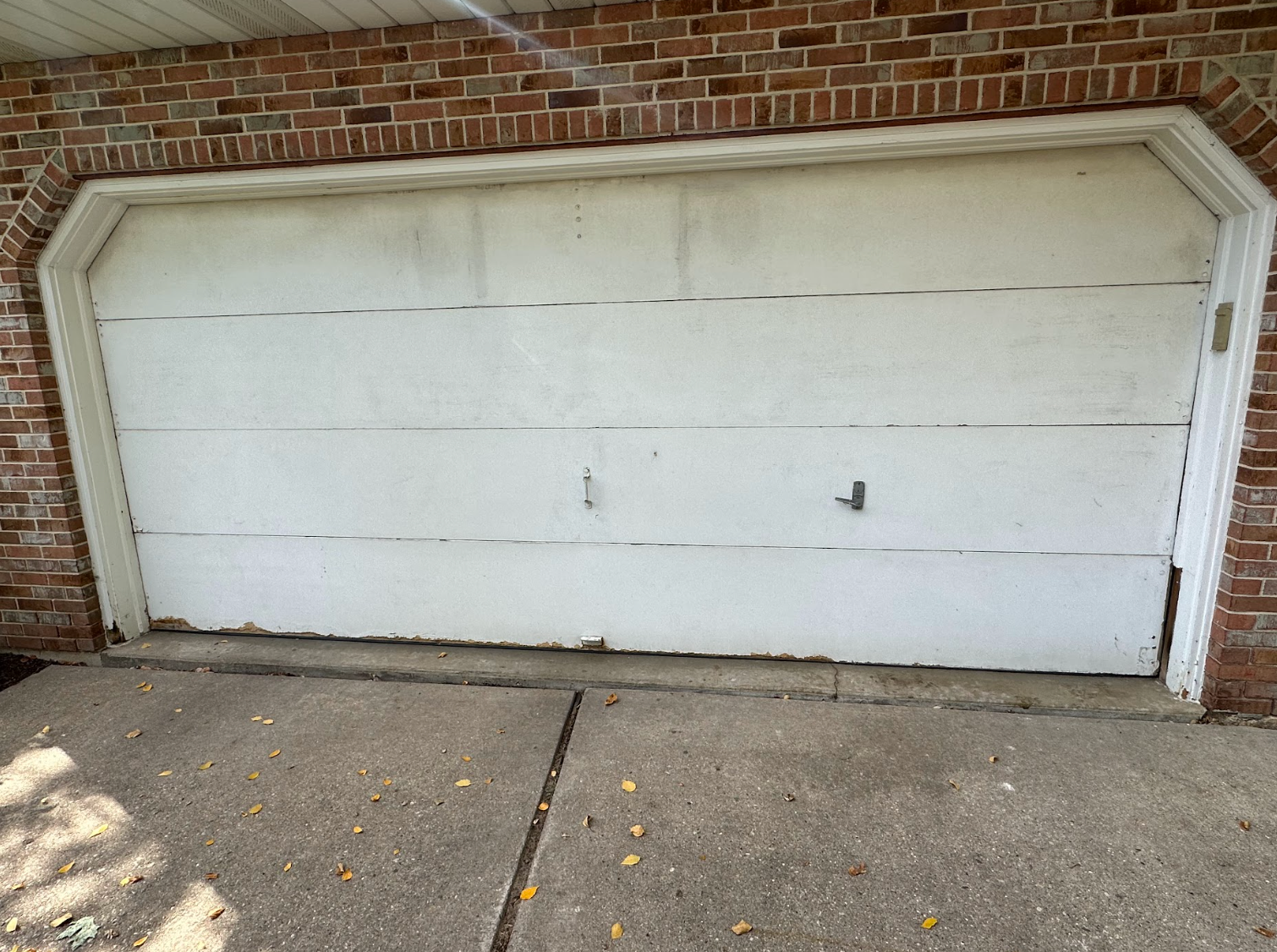 A white garage door with a brick wall behind it
