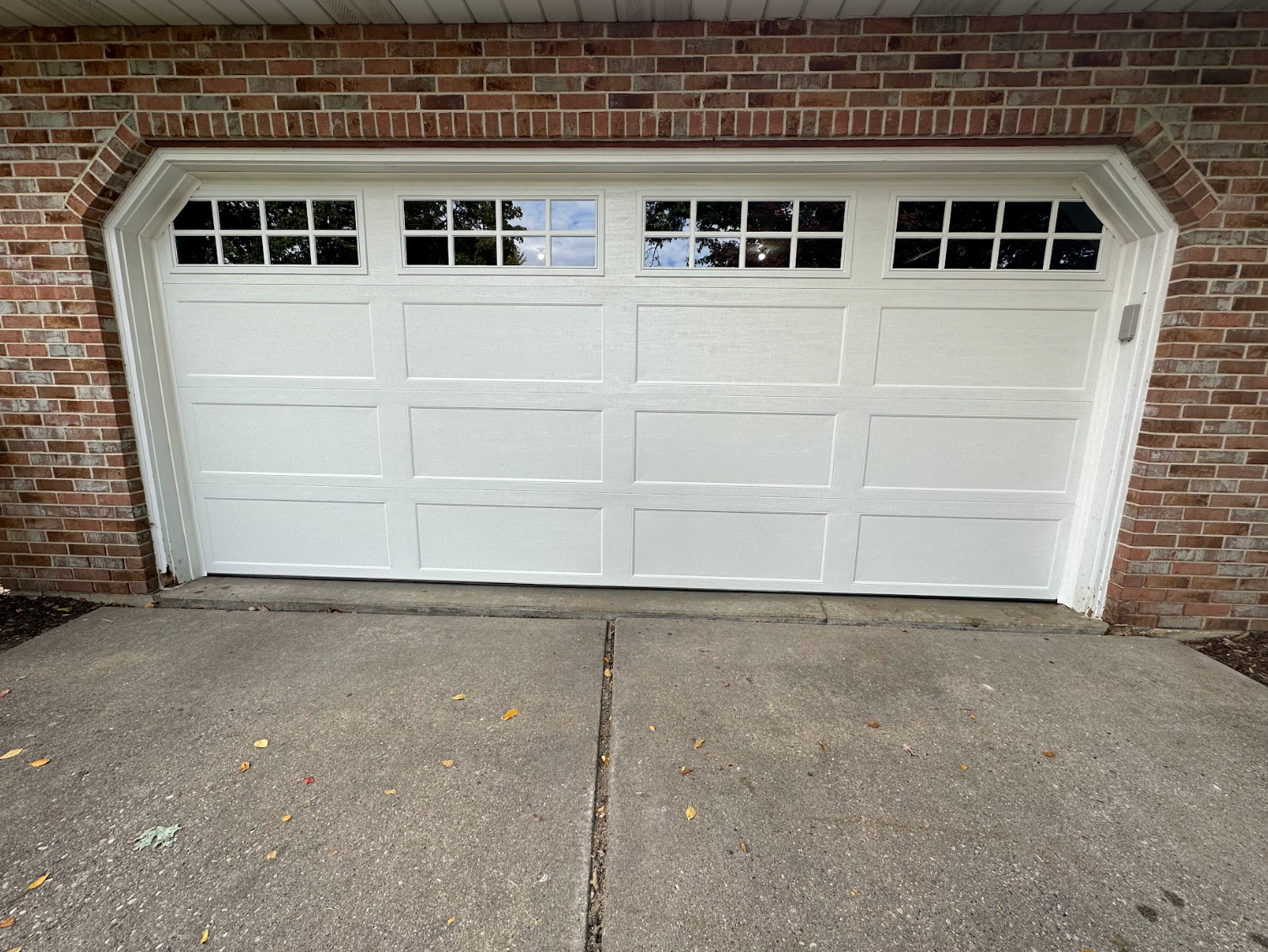 A white garage door is sitting in front of a brick wall.