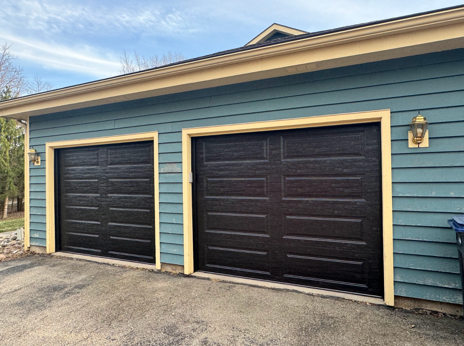A garage with three black garage doors and a blue siding.