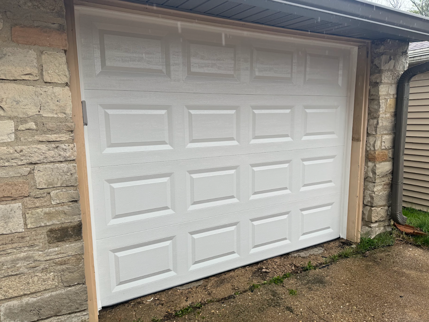 A white garage door is sitting on the side of a stone building.