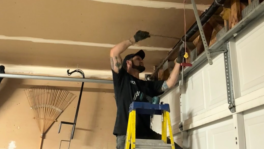 A man is standing on a ladder working on a garage door.