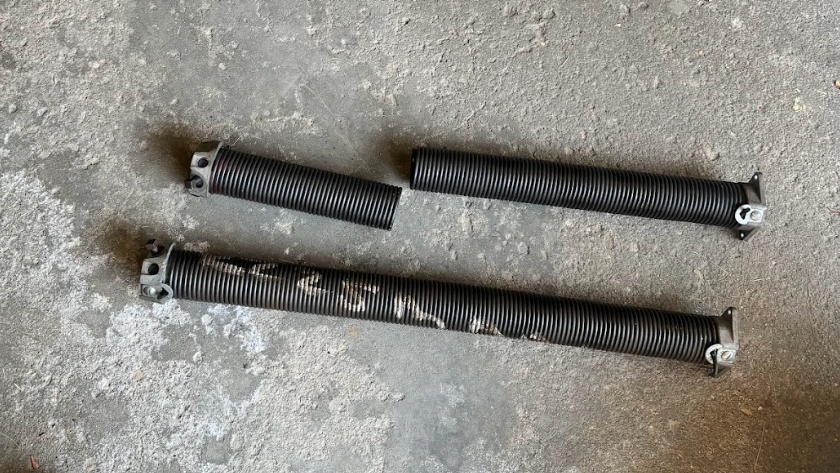 Two broken garage door springs are sitting on a concrete surface.