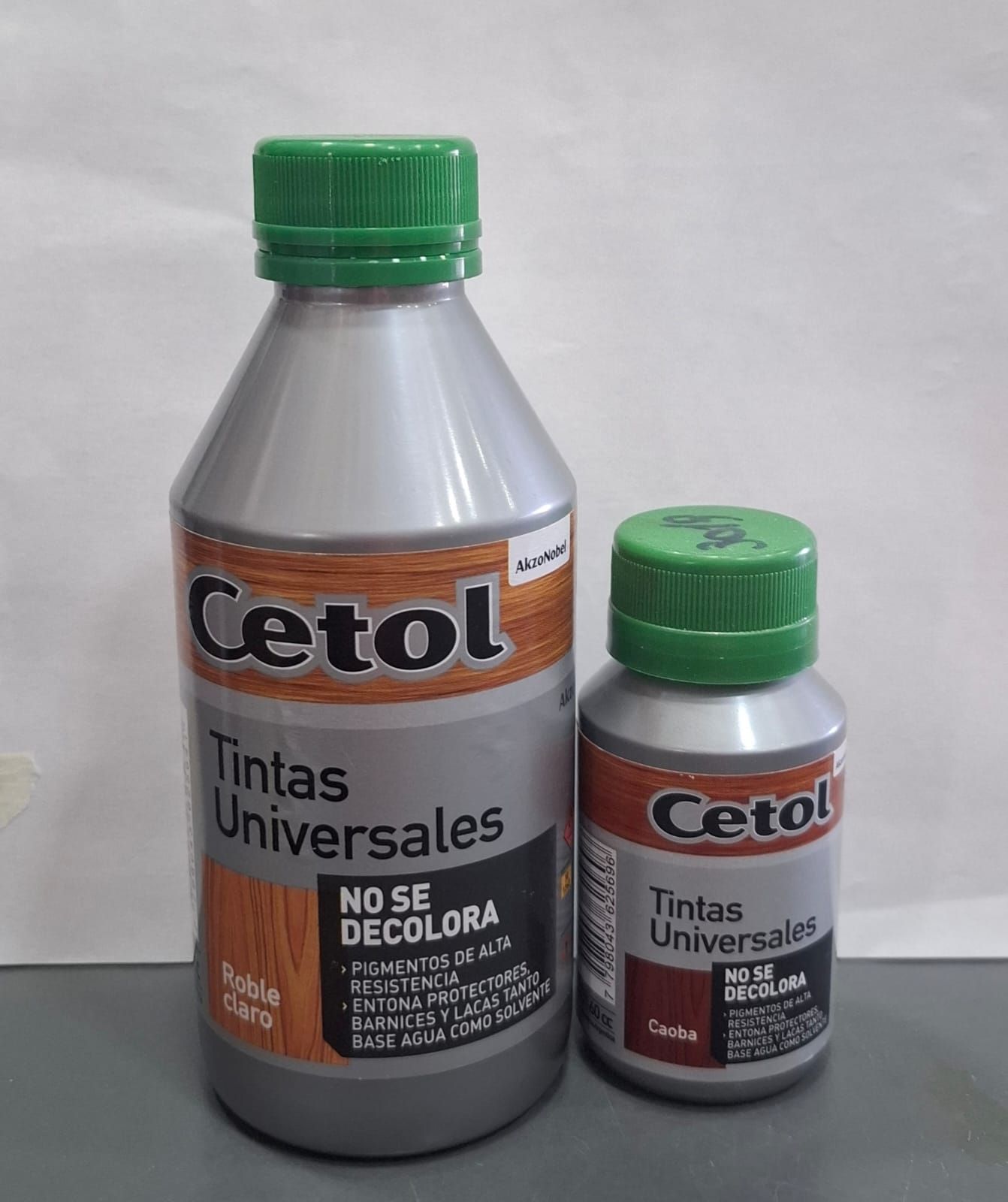 Dos latas de pintura universal Cetol con tapones verdes, una grande y otra pequeña, sobre un fondo liso.