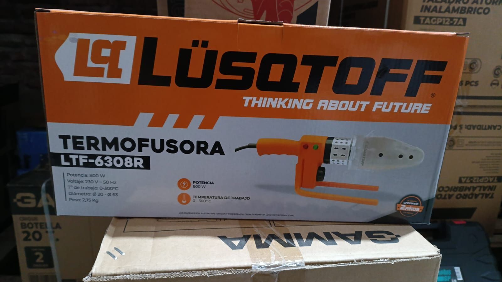 Caja LUSQTOFF TERMOFUSORA LT-6308R con embalaje naranja y blanco sobre cajas apiladas.