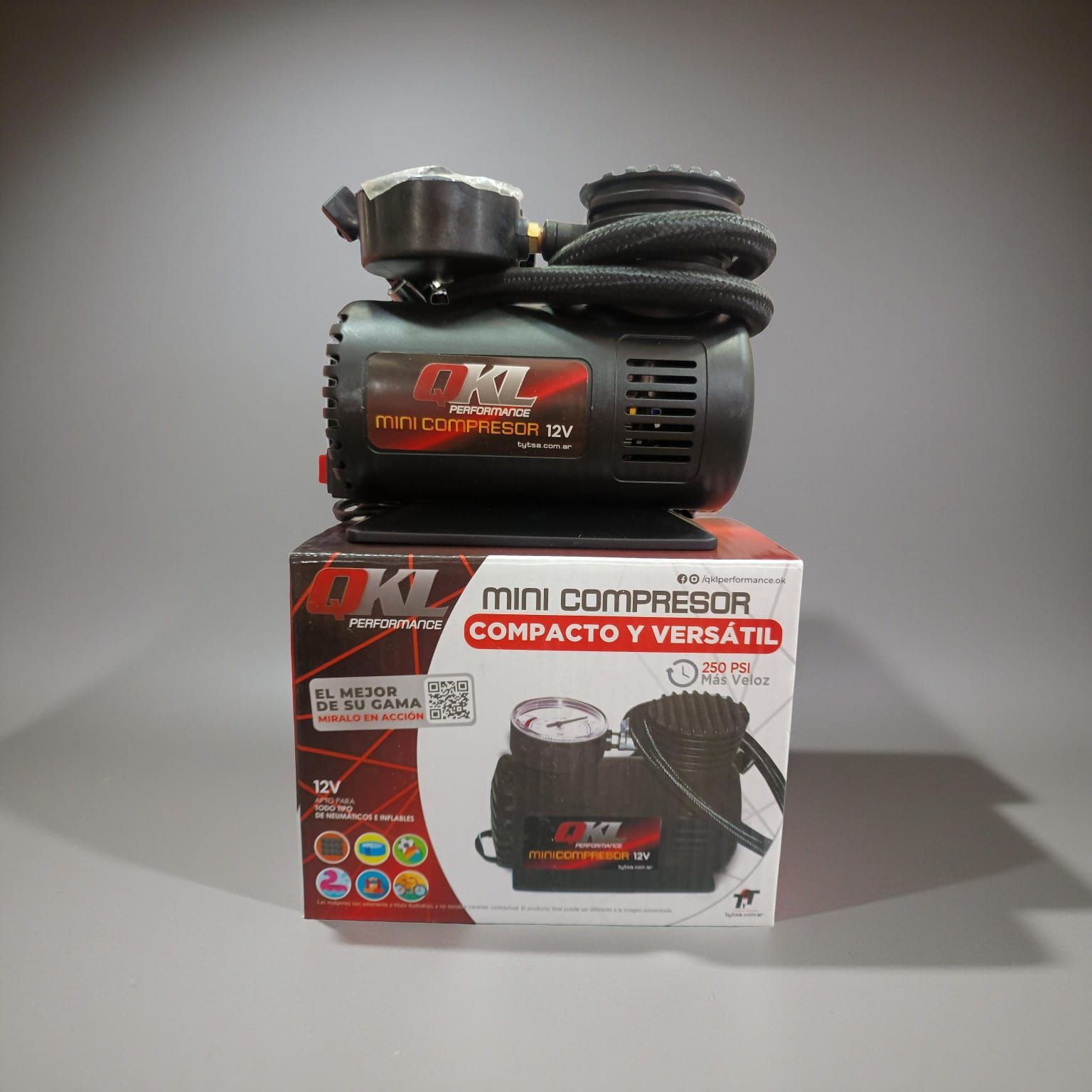 Mini compressor portátil negro y rojo sobre su caja, con manguera enrollada.