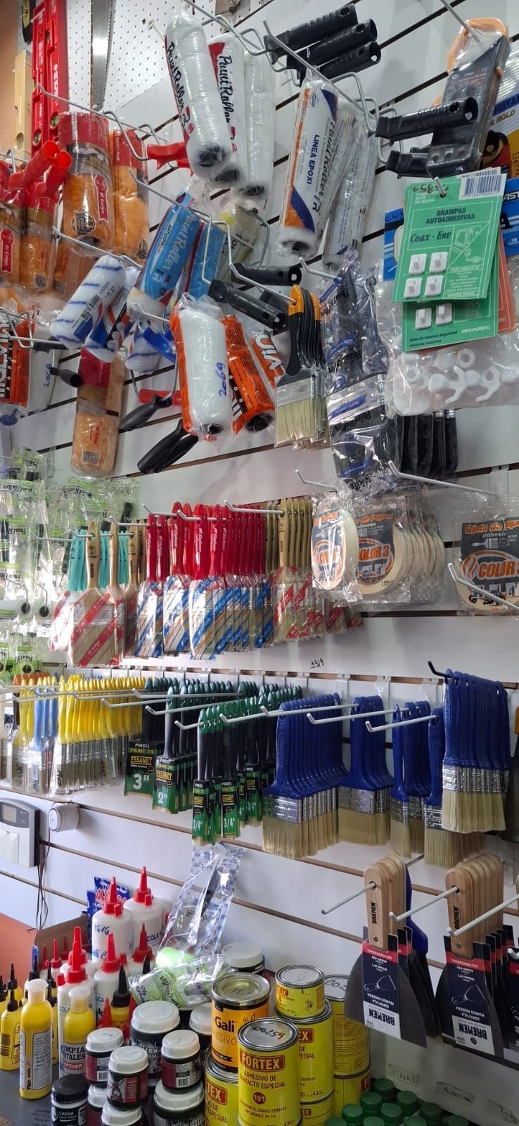 Exhibición de herramientas colgantes, rodillos de pintura, botellas de aerosol y suministros en estantes perforados de una ferretería.