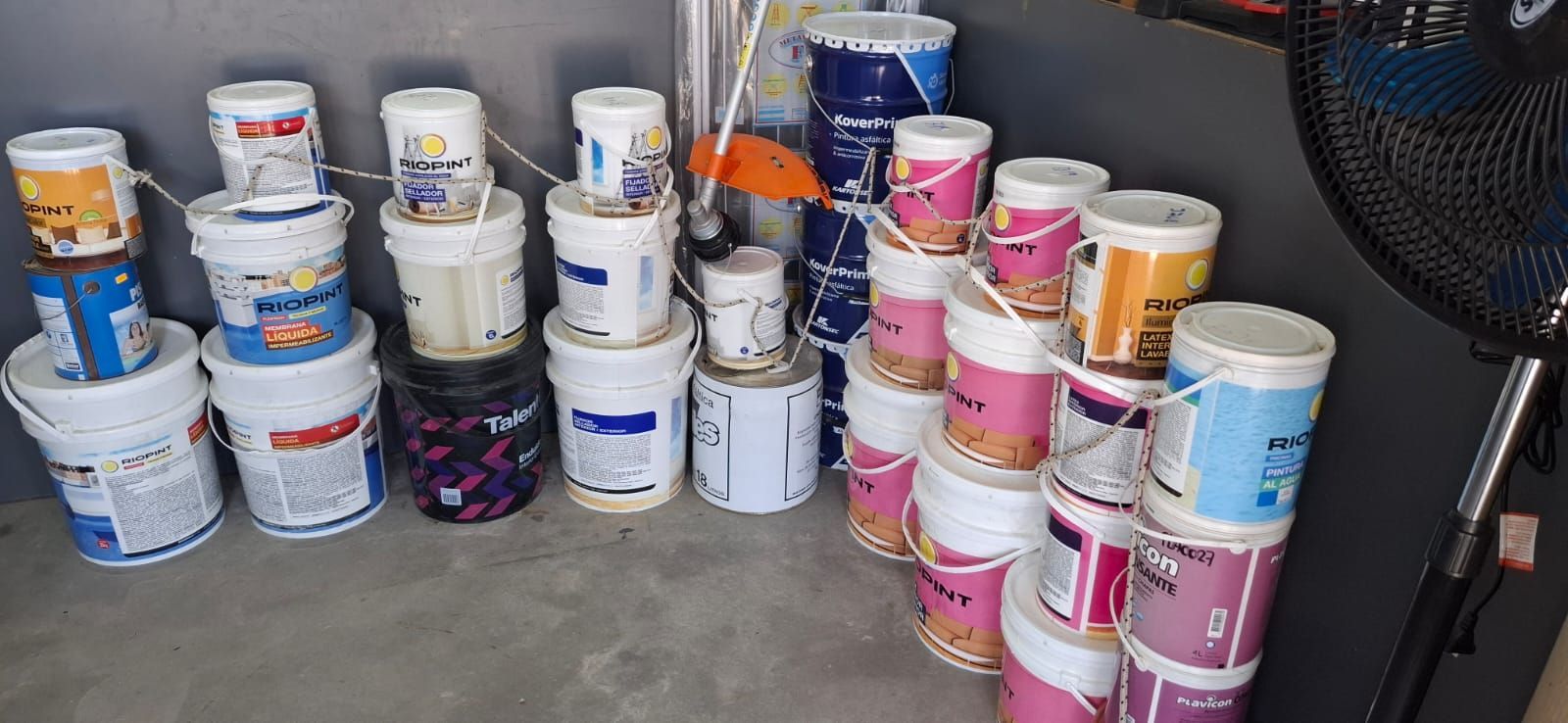 Pilas de cubos de pintura de varios colores alineadas en un suelo de hormigón en un área de almacenamiento.