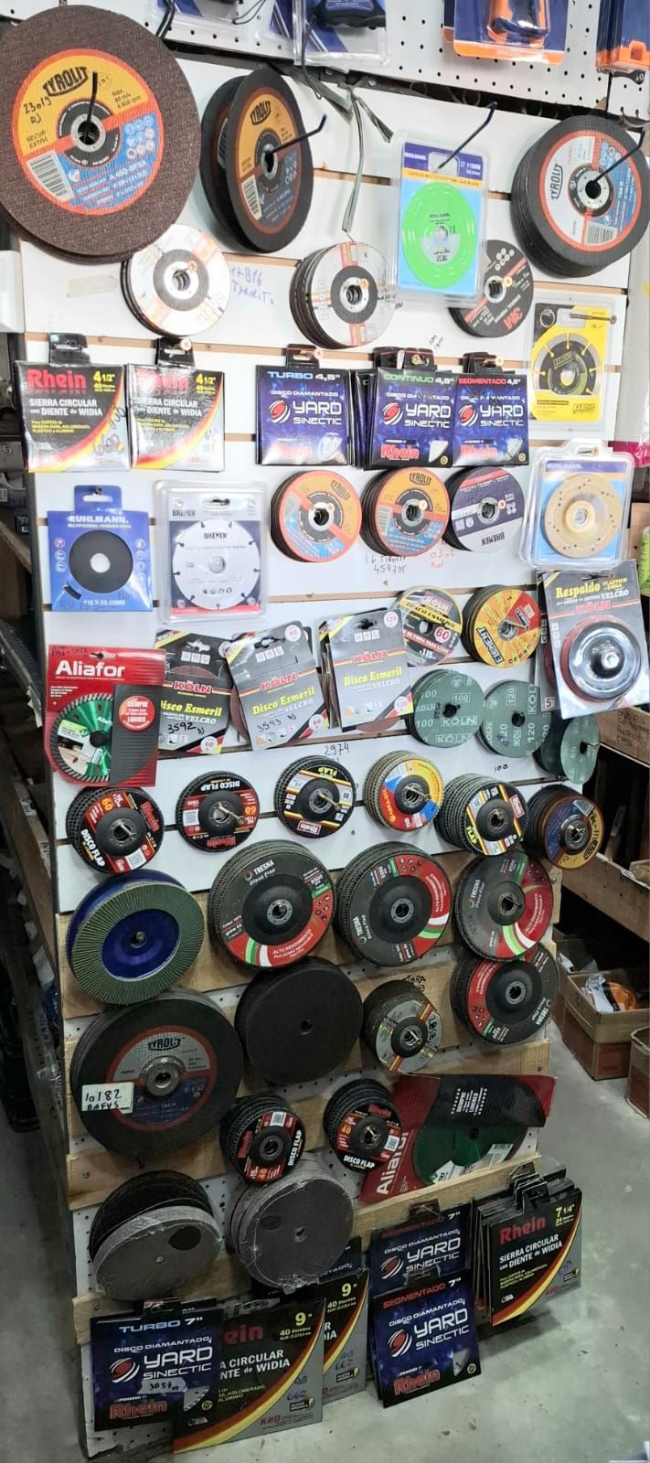 Surtido de discos abrasivos de corte, tanto empaquetados como sueltos, expuestos en la pared y en un estante de una tienda minorista.