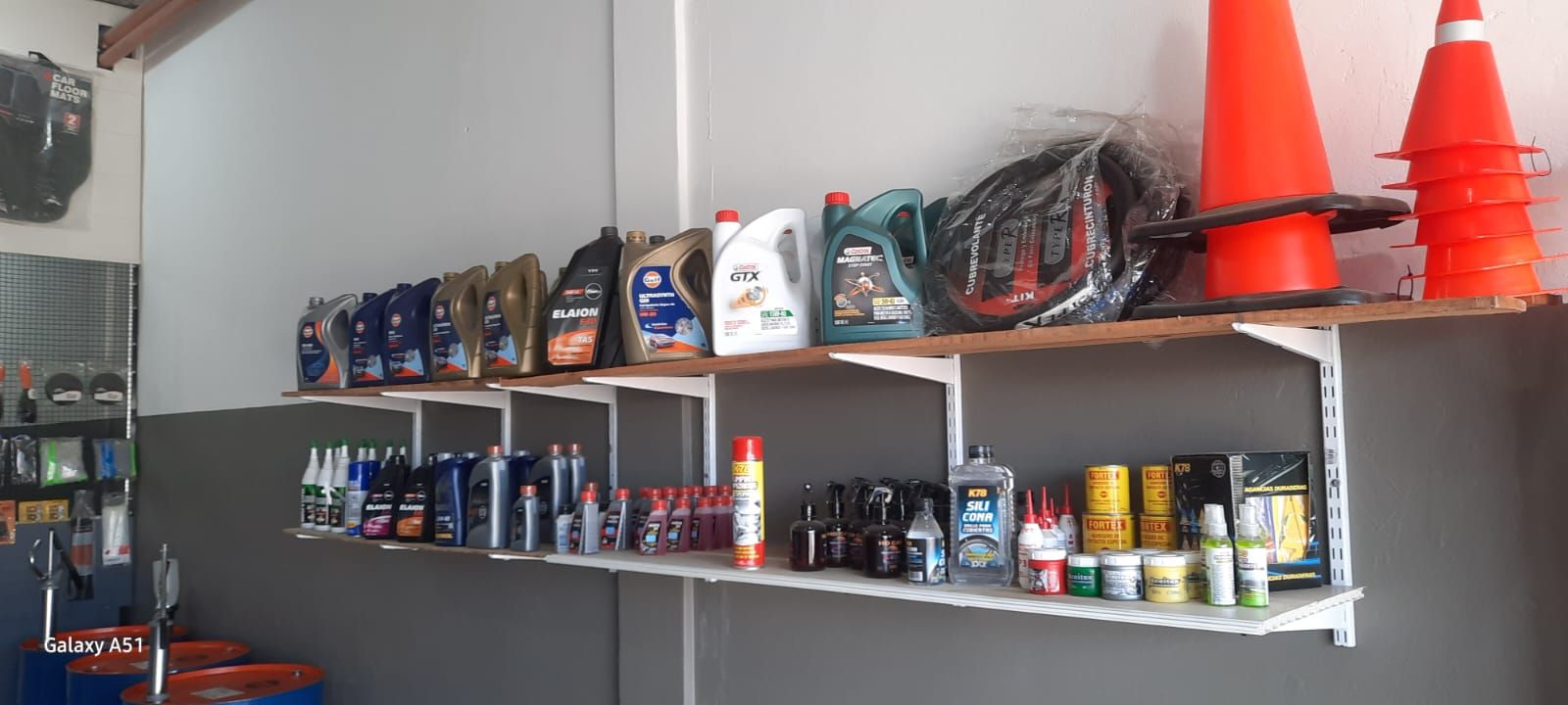 Estanterías repletas de productos para el cuidado del automóvil y conos de tráfico naranjas en un garaje o taller mecánico.