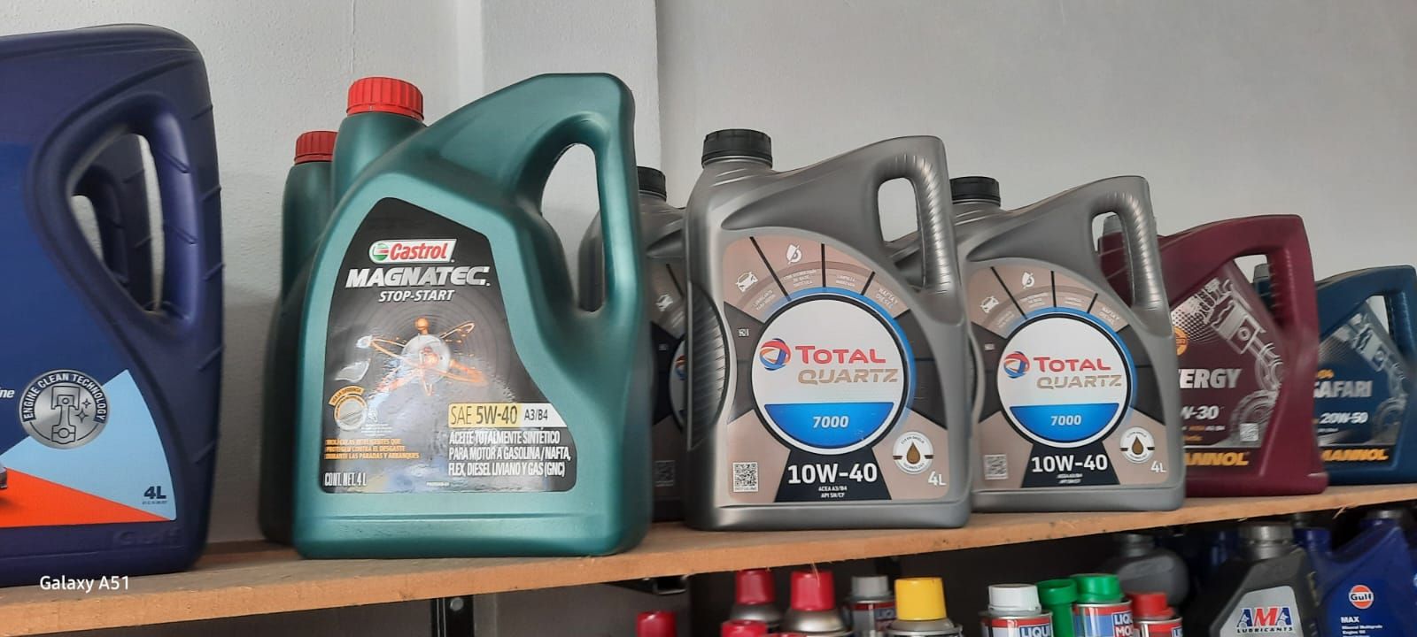 En un estante de una tienda se pueden ver diversos envases de aceite, entre ellos garrafas azules, verdes, grises y rojas.