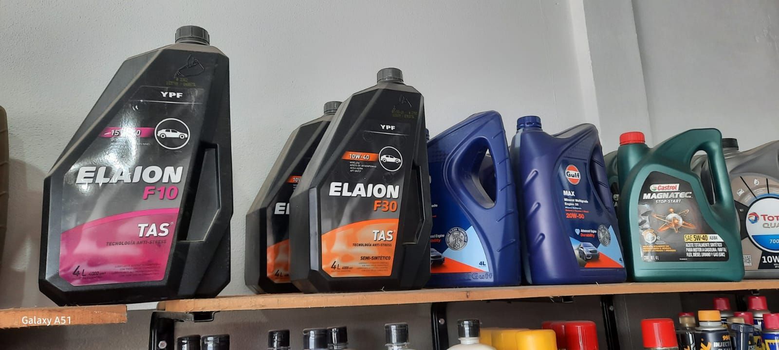 Estantería con botellas de aceite de motor, incluyendo envases negros, naranjas, azules y verdes, en un pasillo de la tienda.