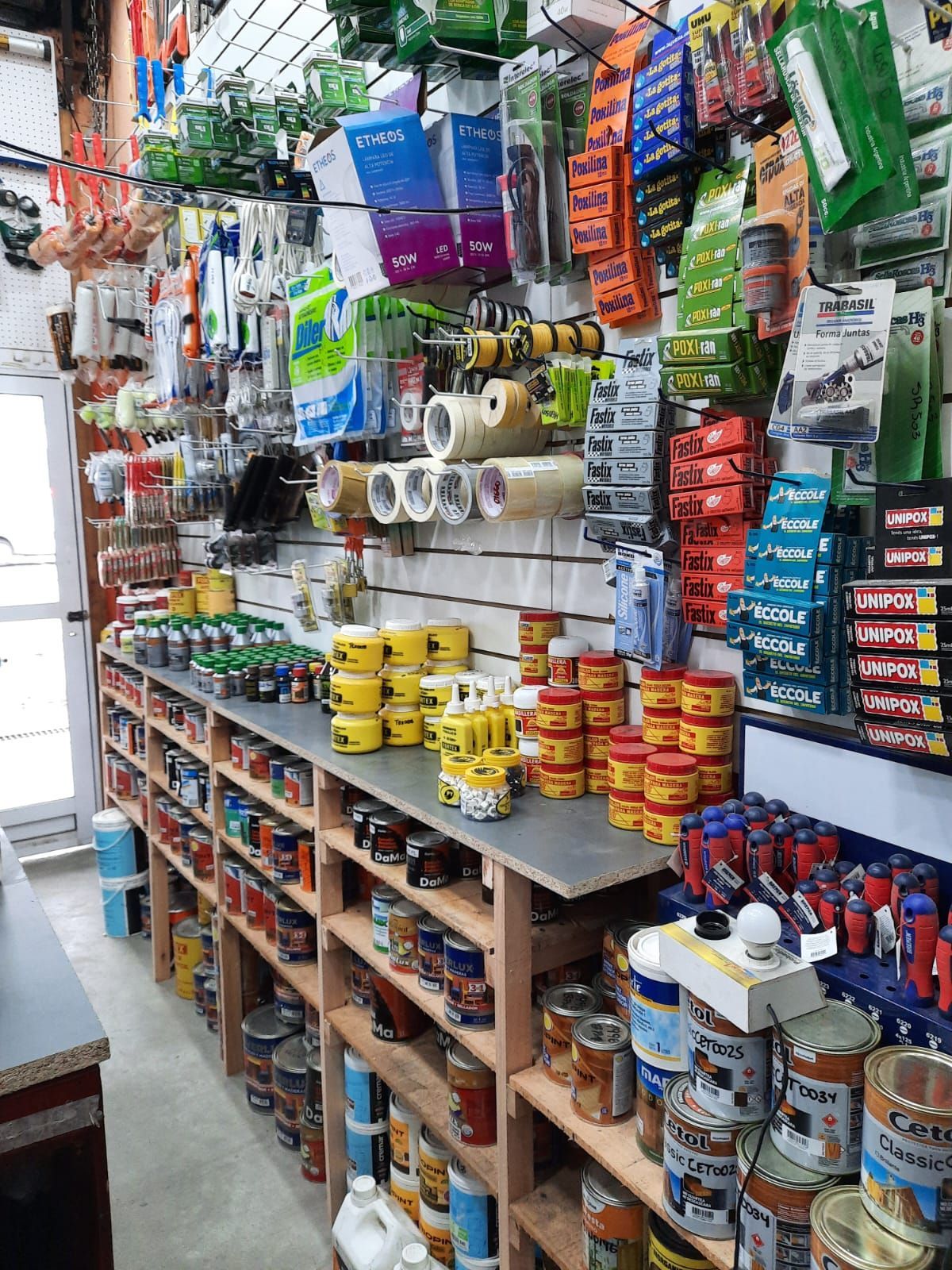 Artículos de ferretería y para el hogar de colores apilados en estantes en un pequeño pasillo de una tienda.