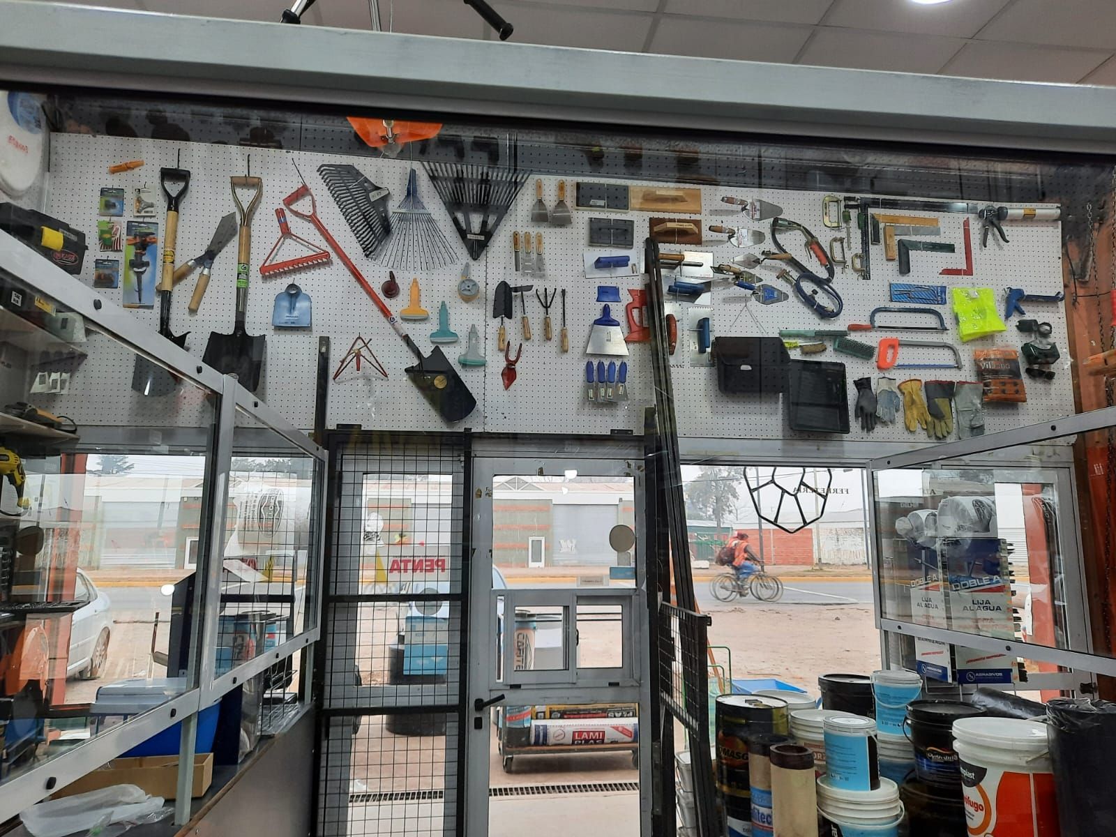 Interior de un taller con herramientas y suministros expuestos en las paredes y estantes cerca de una puerta de cristal.