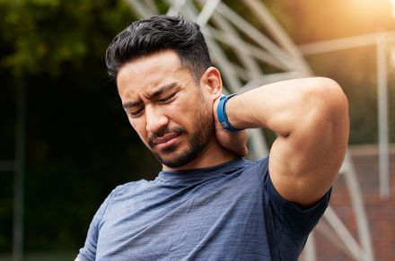 Man holding his neck in pain outdoors near a tennis court fence