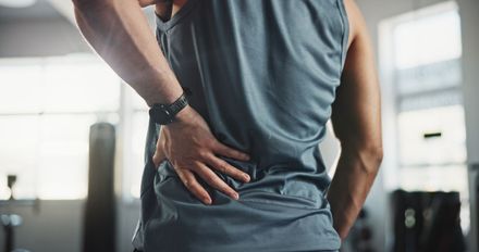 Person in a gray shirt holding their lower back in a gym setting