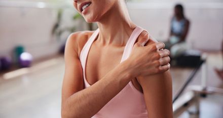 Woman in pink tank top holding her shoulder during a workout in a gym studio