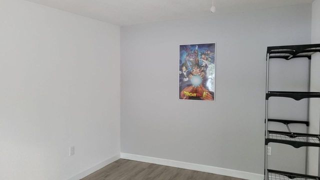 Habitación diáfana y casi vacía, con paredes blancas, suelo gris, cuadros y una estantería de metal negro a la derecha.