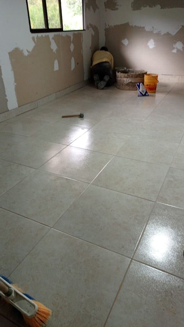 Habitación vacía con suelo de baldosas y paredes sin terminar, una ventana y algunos productos de limpieza en el suelo