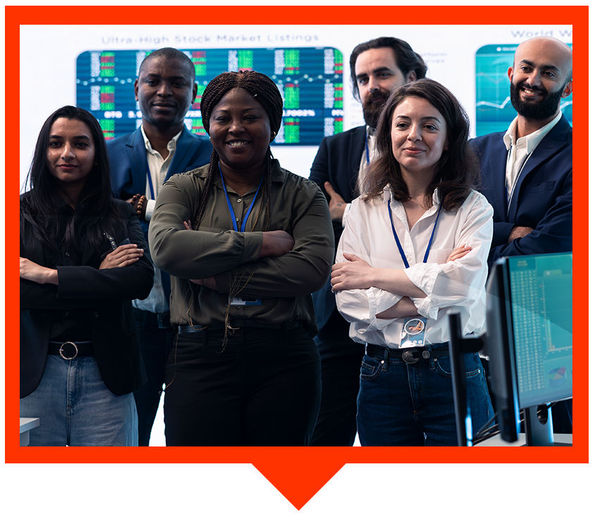 A diverse group of six professionals standing with arms crossed in a modern office with stock market screens in the back.
