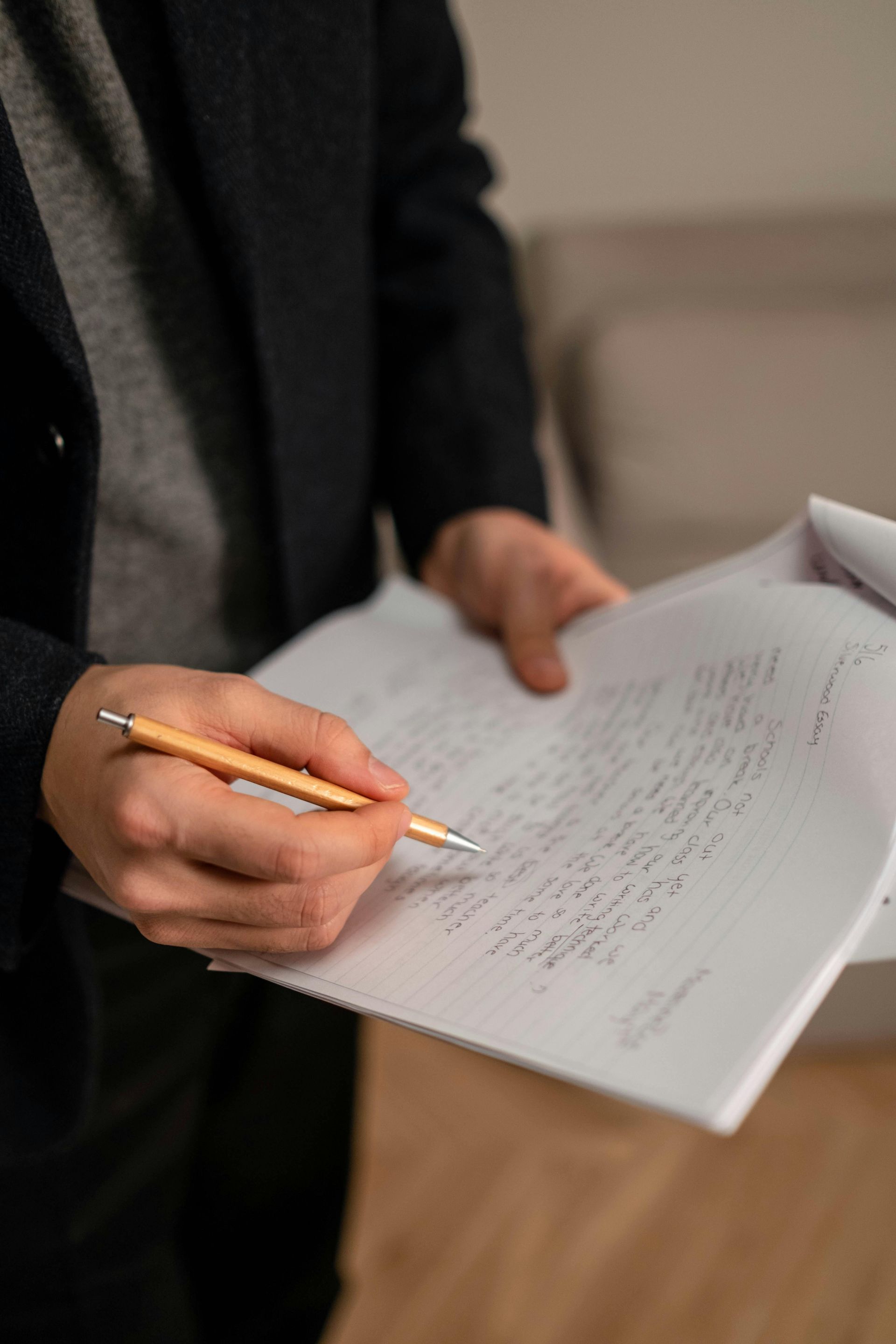 A person in a dark blazer holds a wooden pencil over a sheet of handwritten notes.