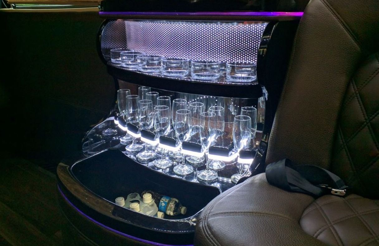 Illuminated custom car interior with rows of glassware and bottles in a luxury console compartment