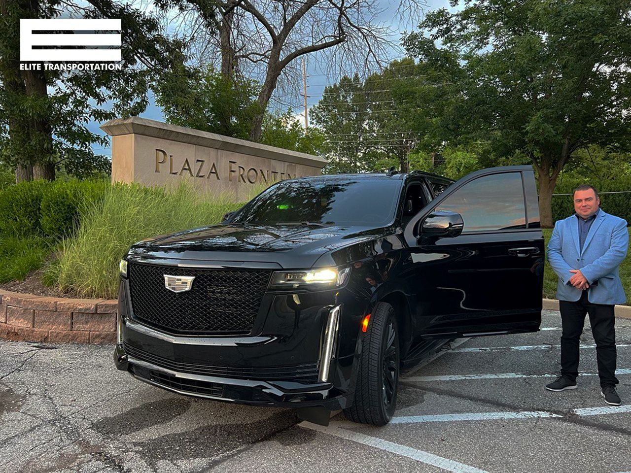 Black Cadillac SUV with an open door, parked at Plaza Frontenac. Man in blue blazer stands beside it.