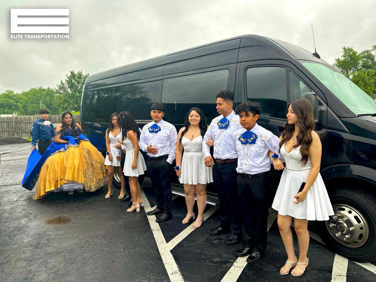 Group of people posing by a black van. They are wearing white or blue outfits.