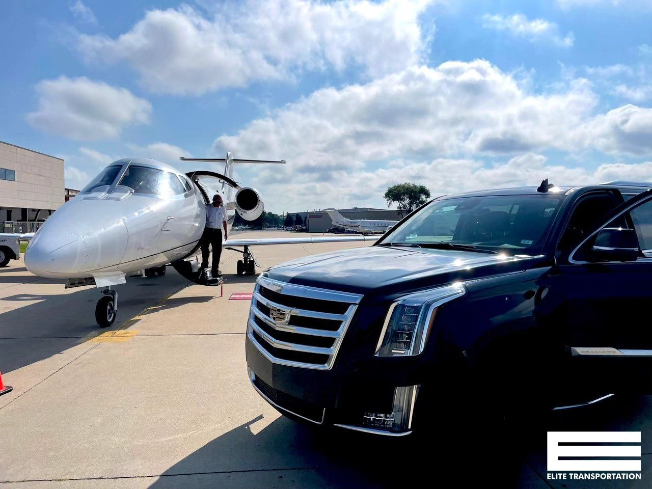 Black SUV parked near a private jet on a sunny tarmac; person standing near the jet.