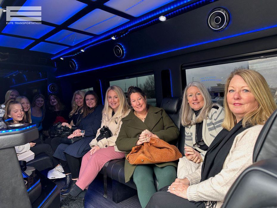 Group of women inside a party bus, smiling. Interior has blue lighting and speakers.