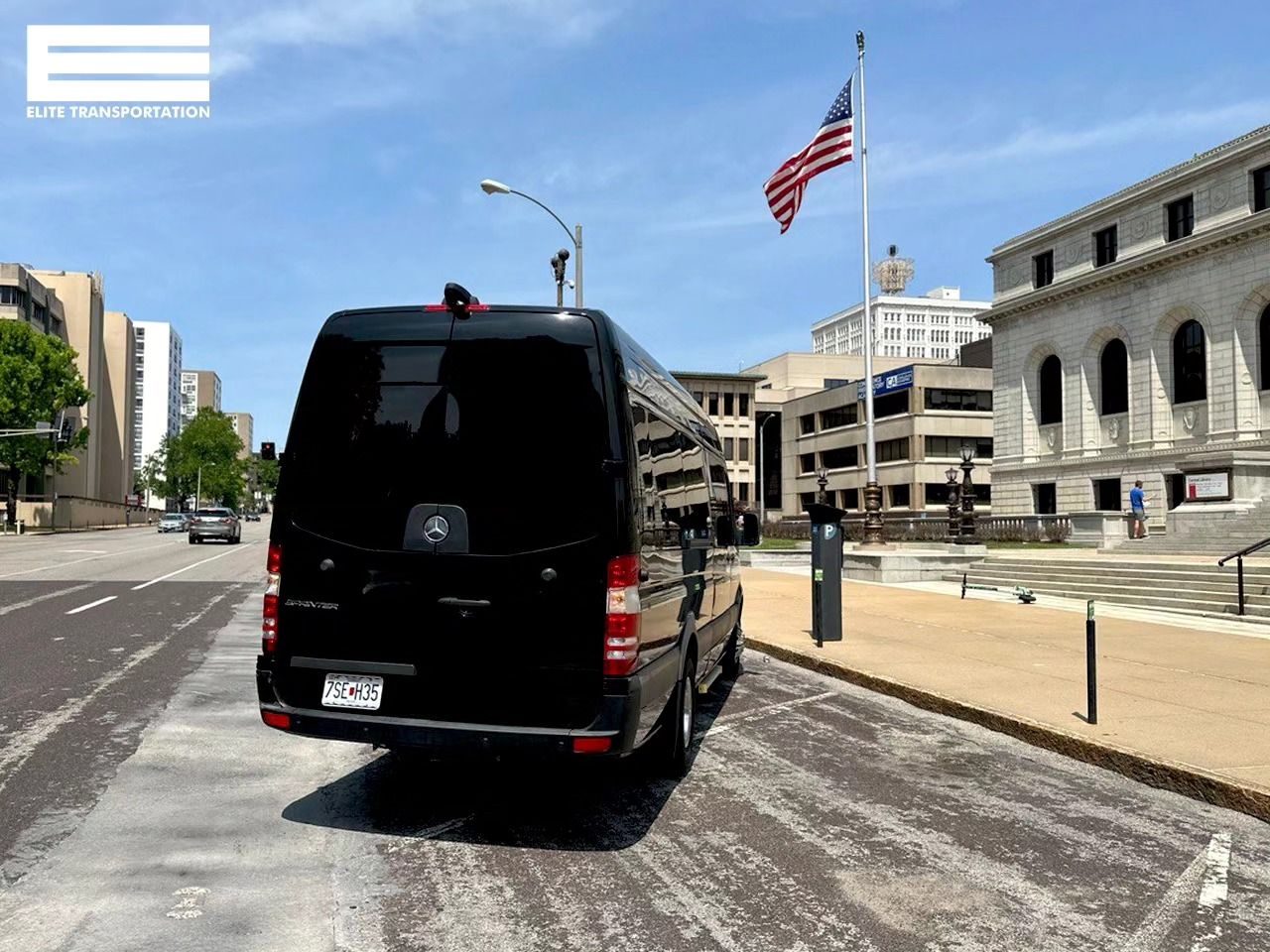 Black van parked on a street near a building with an American flag on a sunny day.