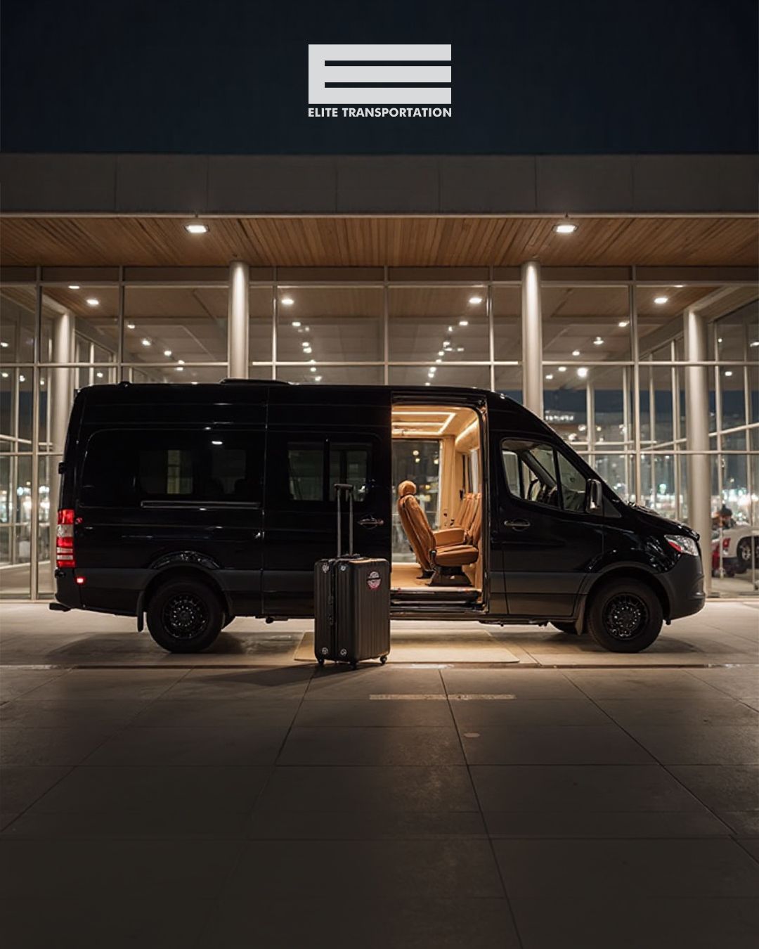 Black van with open sliding door and suitcase parked outside a modern glass building at night