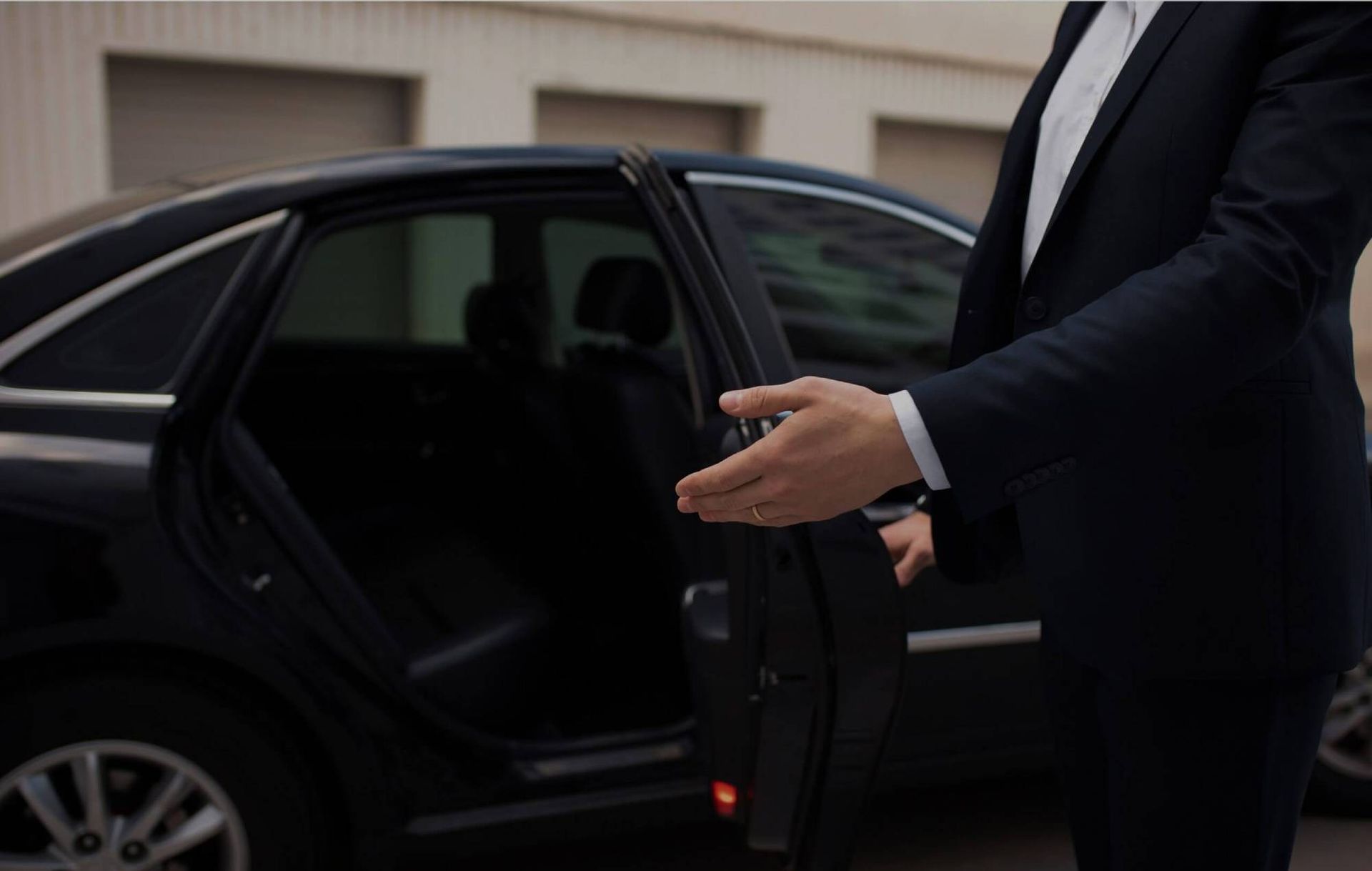 Man in black suit opening the door of a black car outside a building