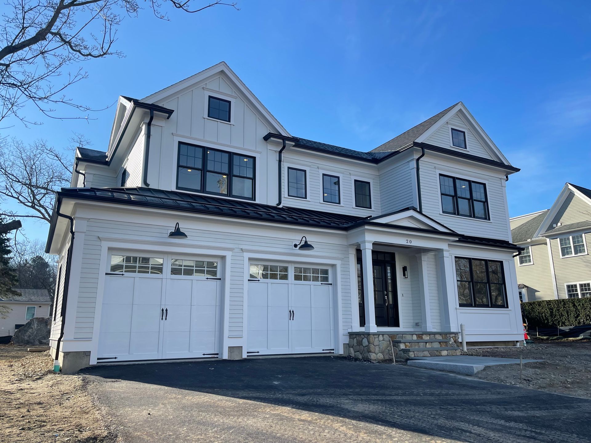 Large white two-story house with black trim, double garage, and a front stone porch under a blue sky