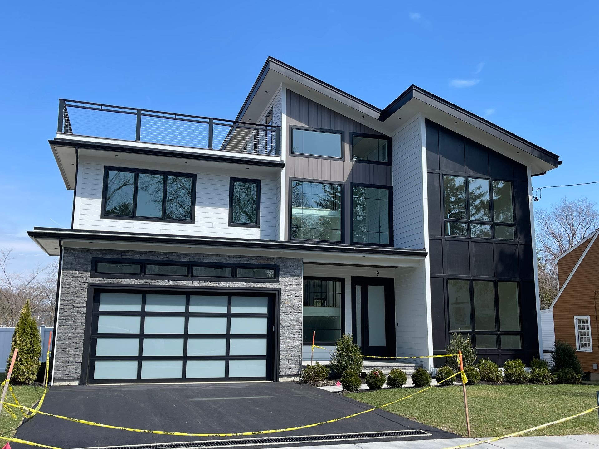 Modern two-story house with black-and-white exterior, large windows, and a garage under a clear blue sky