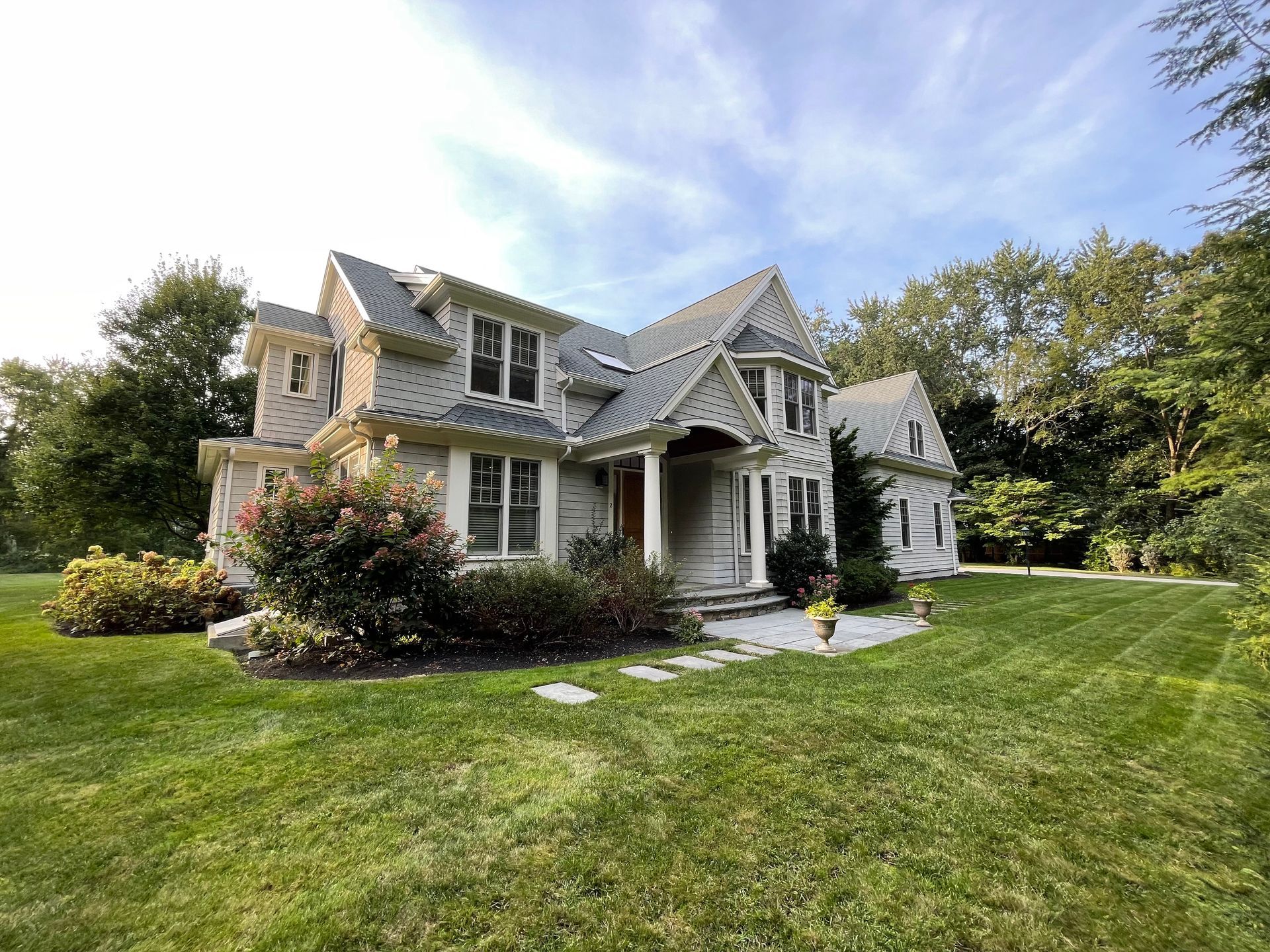 Large white Victorian-style house with a front porch, manicured lawn, and trees on a sunny day