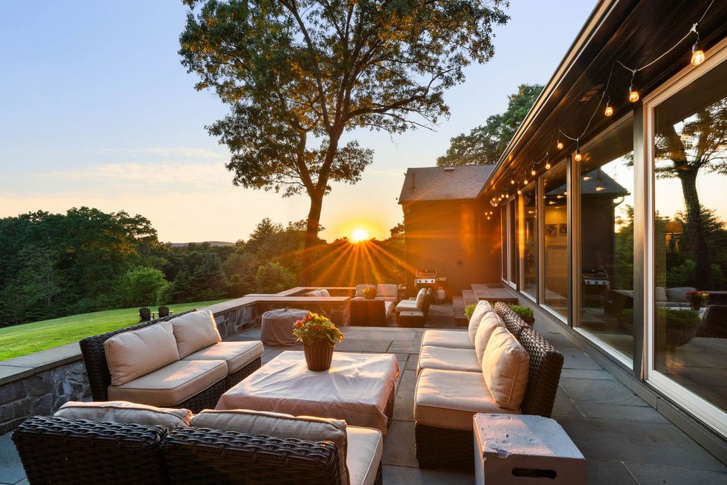 Outdoor patio with sectional seating and string lights at sunset beside a modern house